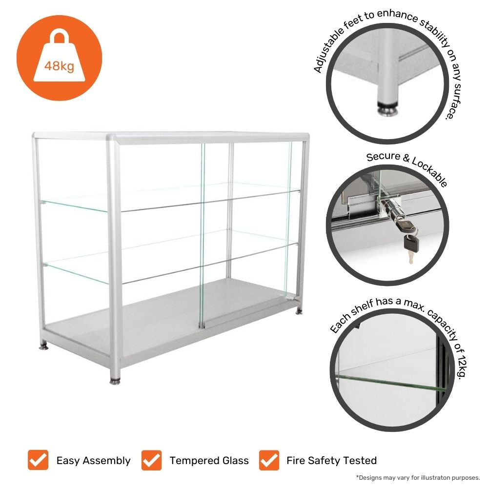 A silver aluminium glass counter display cabinet with two shelves and lockable sliding doors. The cabinet has tempered glass shelves with a maximum capacity of 12kg each. It features adjustable feet for stability on various surfaces and a secure lockable door. The total weight of the cabinet is 48kg. Additional icons highlight its easy assembly, tempered glass construction, and fire safety testing. The design may vary slightly from the illustration.