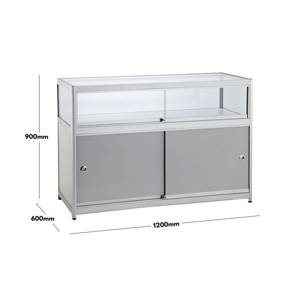 A silver aluminium glass counter display cabinet with dimensions of 1200mm in width, 600mm in depth, and 900mm in height. The cabinet features a tempered glass top display section with a lockable sliding door and a secure lower storage compartment with sliding doors. Its modern and functional design is suitable for retail and exhibition use, providing both display and storage space.