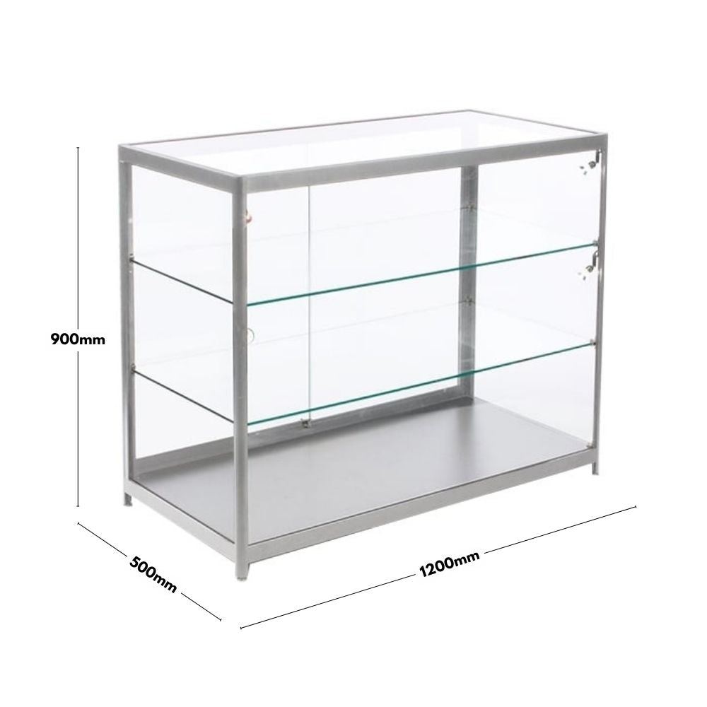  A silver aluminium glass counter display cabinet with dimensions of 1200mm in width, 500mm in depth, and 900mm in height. The cabinet features a sturdy aluminium frame with tempered glass panels and two glass shelves for display. It has lockable sliding doors for security. The design is sleek and modern, suitable for retail or exhibition use.