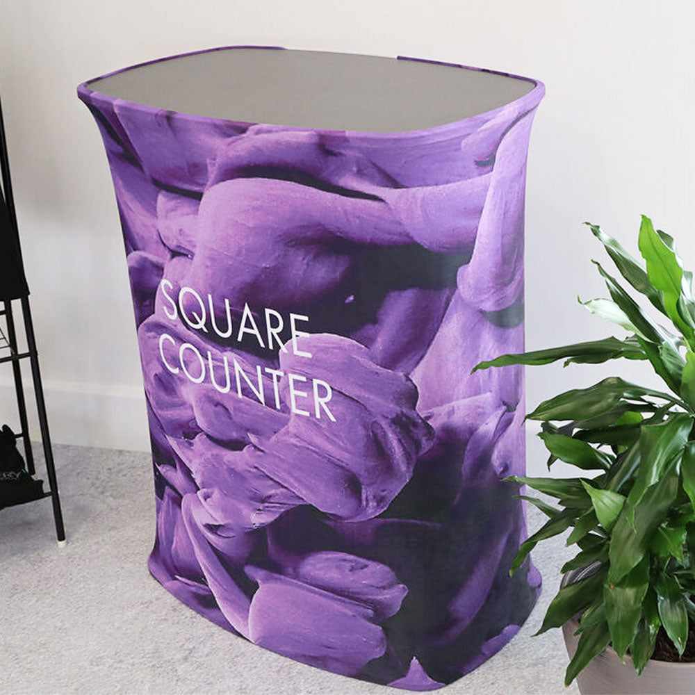 This sturdy square exhibition counter, measuring 800mm, features a durable fabric body with a stylish black wooden top and includes a high-quality graphic printing service for personalised marketing.
